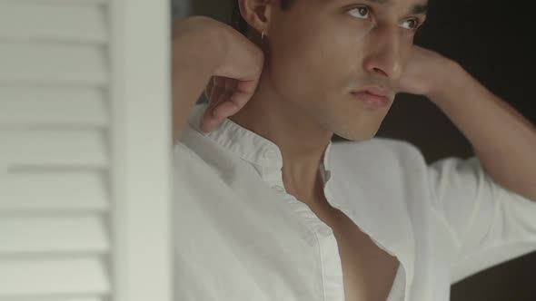 Attractive young man dresses a stylish white cotton shirt at home. Slow motion