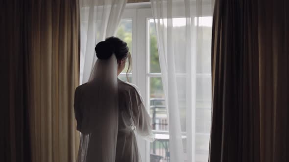 Bride in White Boudoir Dress Going To Balcony and Opens Curtains and Door in Hotel Room Apartment