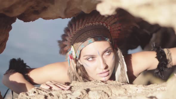Ethnic Wonderful Woman with Native American Headdress and Ornament Hiding in Rocks Hunting Eyes