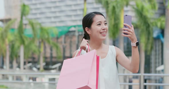 Woman make video call on cellphone with holding lots of shopping bag