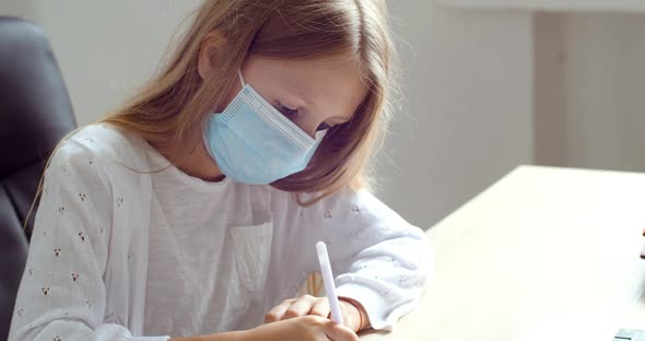 Little Girl in Protective Medical Mask on Her Face Writing with Pen in Notebook, Doing Homework