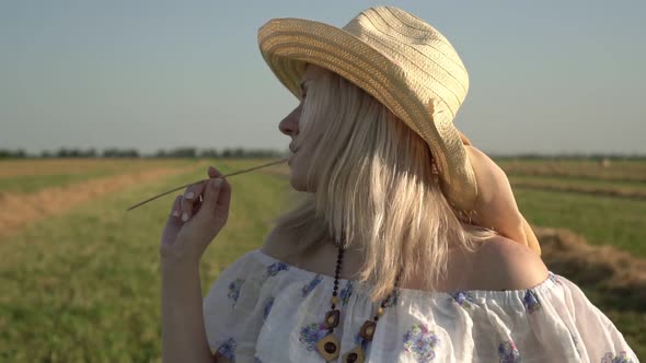 Portrait of a Happy Rural Woman in a Straw Hat and Summer Dress on a Green Field Background