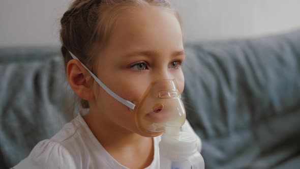 Little Girl Makes Inhalation with Medical Nebulizer While Sitting on Bed