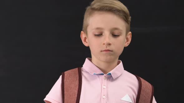 Upset Schoolboy With Rucksack Looking at Camera Isolated on Black Background