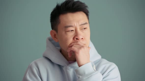 Pensive Asian man wearing hoodie thinking about something and positively shaking his head