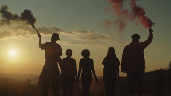 Silhouette of Carefree Diverse People with Smoke Bombs Walking on Mountain Top at Sunset