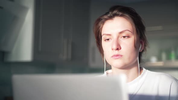 A Beautiful Freelancer Girl Works in Her Kitchen Behind a Laptop and Listens To Music Through