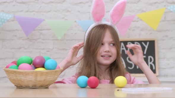 Funny Easter Kid Girl with Bunny Ears Steals Eggs From the Table