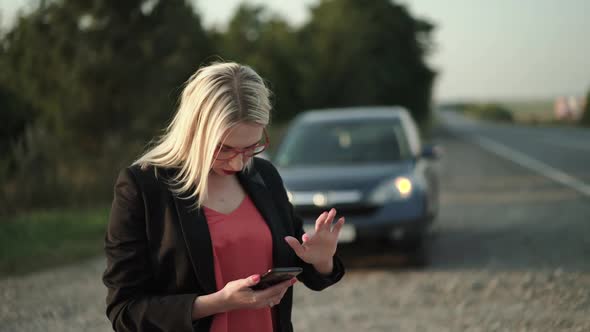 Confused Lady Flips Through the Phone Screen and Looks Around at Broken Car
