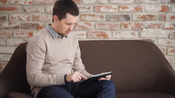 The Man Prints Text on a Tablet, He Holds a Gadget in Hand and Uses the Internet