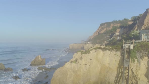 Aerial shots of El Matador beach over breaking waves and rocks on a hazy summer morning in Malibu, C