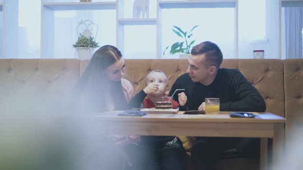 Happy Couple Looks at Eating Child and Mother Kisses Kid