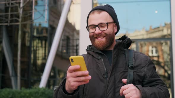 Handsome Bearded Man in 30s Looking at Phone Screen and Laughing While Walking at Street. Cheerful