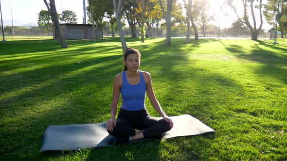 A young woman doing yoga in meditation pose in nature at sunrise to reduce anxiety and stress.