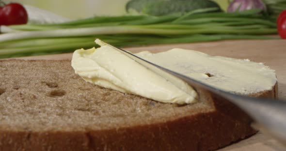 Butter Spread Is Spreading On A Bread Slice With A Knife On A Cutting Board With Vegetables