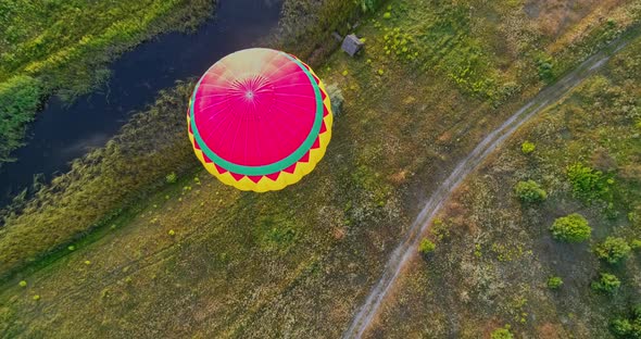 Aerostat on nature background. Colorful hot air balloon flying over the field near the small river. 