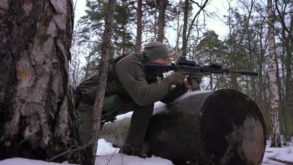 Panning Shot of Young Concentrated Sniper Aiming with Gun in Winter Forest in Slow Motion