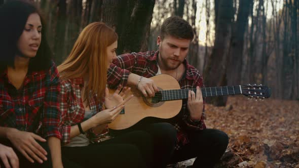 Young Tourist Tuning Guitar By Campfire in Autumn Forest