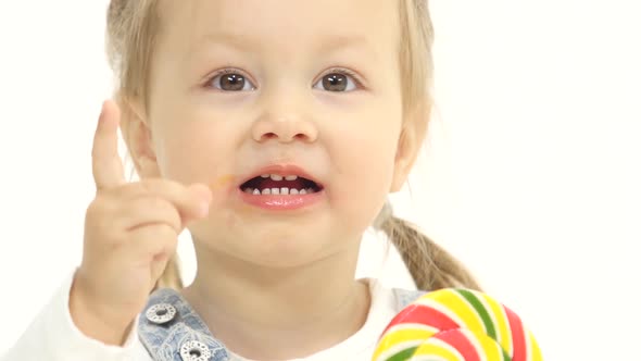 Child Is Holding a Sweet Candy in Her Hands and Licks It. White Background. Close Up