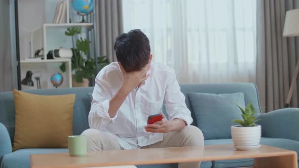 Asian Man Being Tired While Using Smartphone In The Living Room