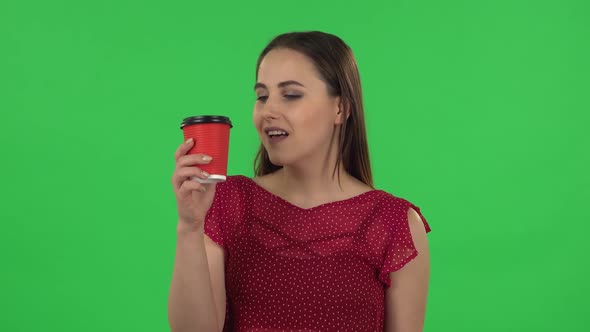 Portrait of Tender Girl in Red Dress Drinking Unpalatable Coffee and Is Disgusted