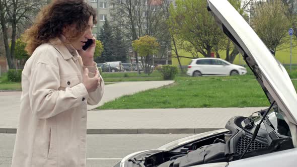 Middleaged Woman Driver Stands Near the Open Hood of Her Car