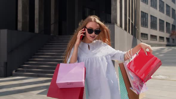 Girl Walking From Mall with Shopping Bags and Talking on Mobile Phone About Sale on Black Friday