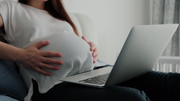 Close Up of Pregnant Woman Resting on a Sofa at Home and Working Remotely with Laptop Computer Using