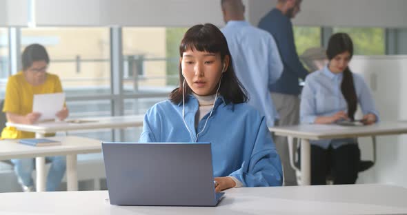 Young Asian Businesswoman Using Laptop and Headphones Having Video Call at Office