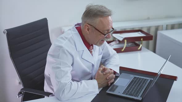 Male doctor working at office desk. Doctor therapist speaks with patient video chat using laptop 