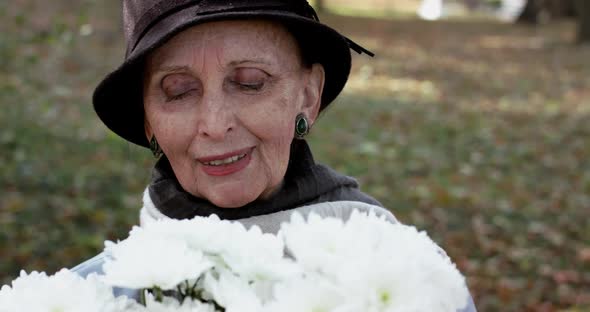 Elderly Lady in Hat Enjoying From Bouquet's Smell and Smiling Into Camera