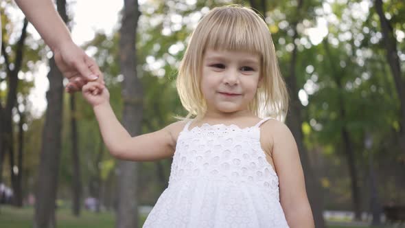 A Little Girl in White Dress Standing in the Park or Forest Holding Hand of the Adult Woman