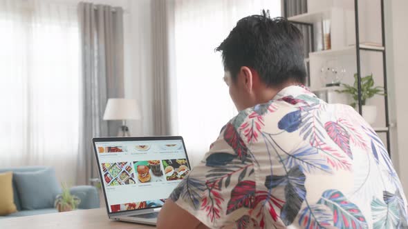 Asian Man Using Laptop Computer And Doing Online Shopping At Home, Male Looks At Food For Order