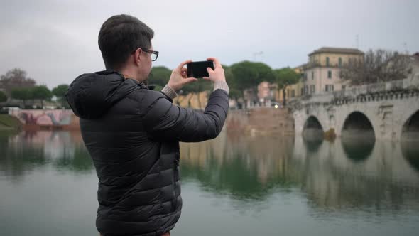 Man Films Ancient Bridge of Tiberius Arches Over Calm River