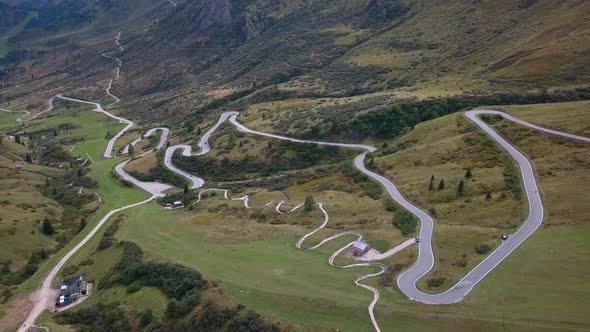 Long winding road in the Dolomite mountain range northern Italy with carsing near the meadow, Aerial