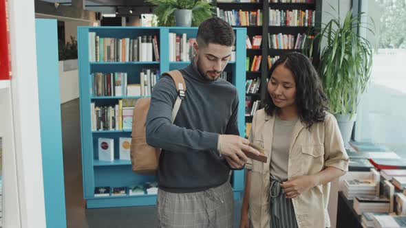 Two University Students Discussing Book in Library