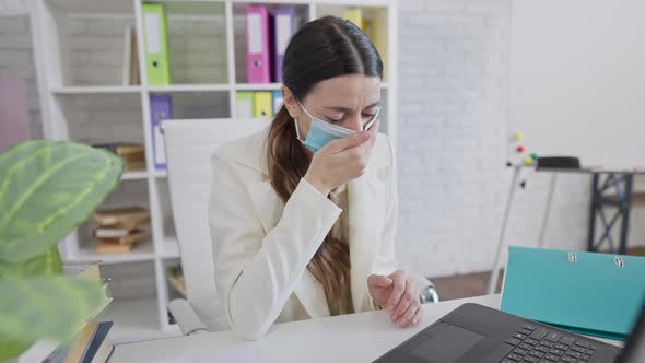 Ill Young Caucasian Woman in Coronavirus Face Mask Sneezing and Coughing Sitting at Laptop in Office