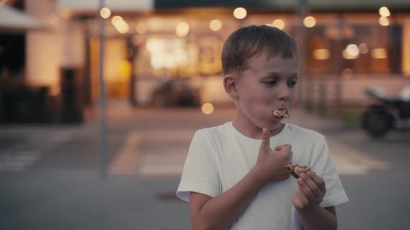 Hungry Young Boy Eating a Burger on the Evening Street