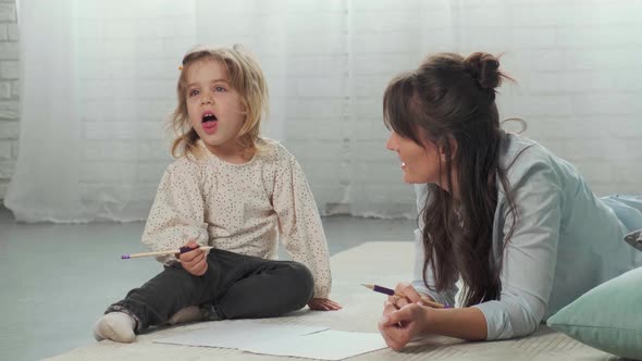 Mom and Daughter Lying on Carpet on the Floor Drawing on Paper and Having Fun