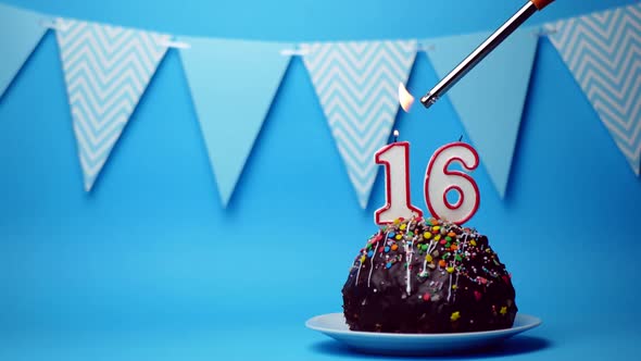 Chocolate Birthday Cake with a Burning Candle Number Sixteen 16 on a Blue Background