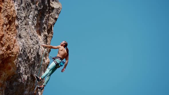 Strong Muscular Handsome Man Hanging on Rope on Rock Climbing Route Resting and Reaching Holds and