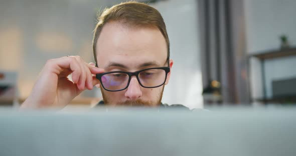 Man in Glasses which Sitting at his Workplace in front of Laptop 