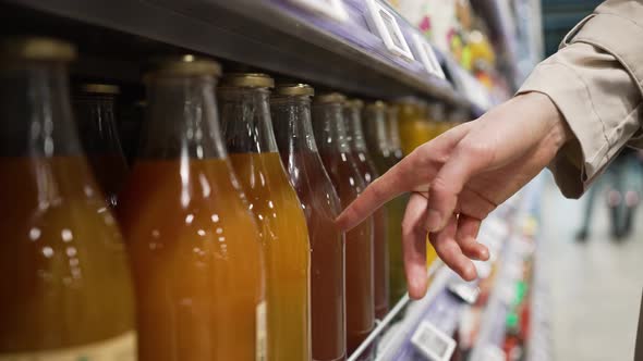 Woman's Hand Chooses Fruit Juice in a Glass Bottle in a Grocery Supermarket Closeup