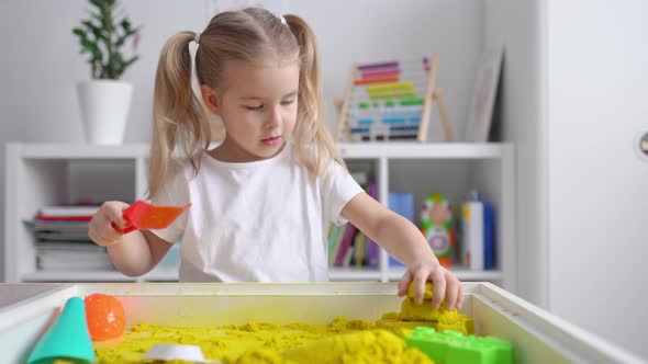 Little blonde girl with two ponytales play with yellow magic sand