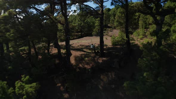 Aerial pull back girl running to the edge of the cliff between trees