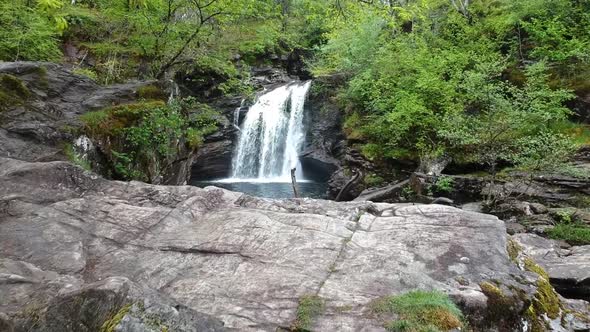 Fly-over drone shot of mountain waterfall with river