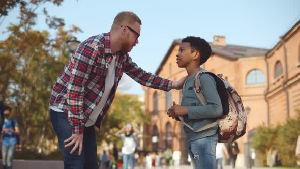 Side View of Male Teacher Talking To Preteen African Schoolboy Outdoors
