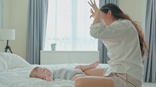 Caucasian loving mom play with cute baby boy child on bed in bedroom.