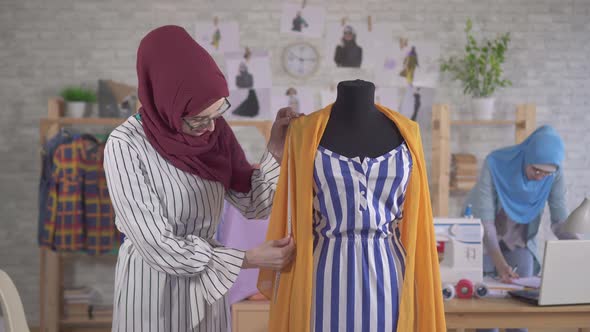 Young Muslim Woman Fashion Designer in National Headscarf Takes Measurements with a Tape Measure