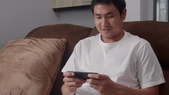 Young Asian man using mobile phone playing video games in television in living room.